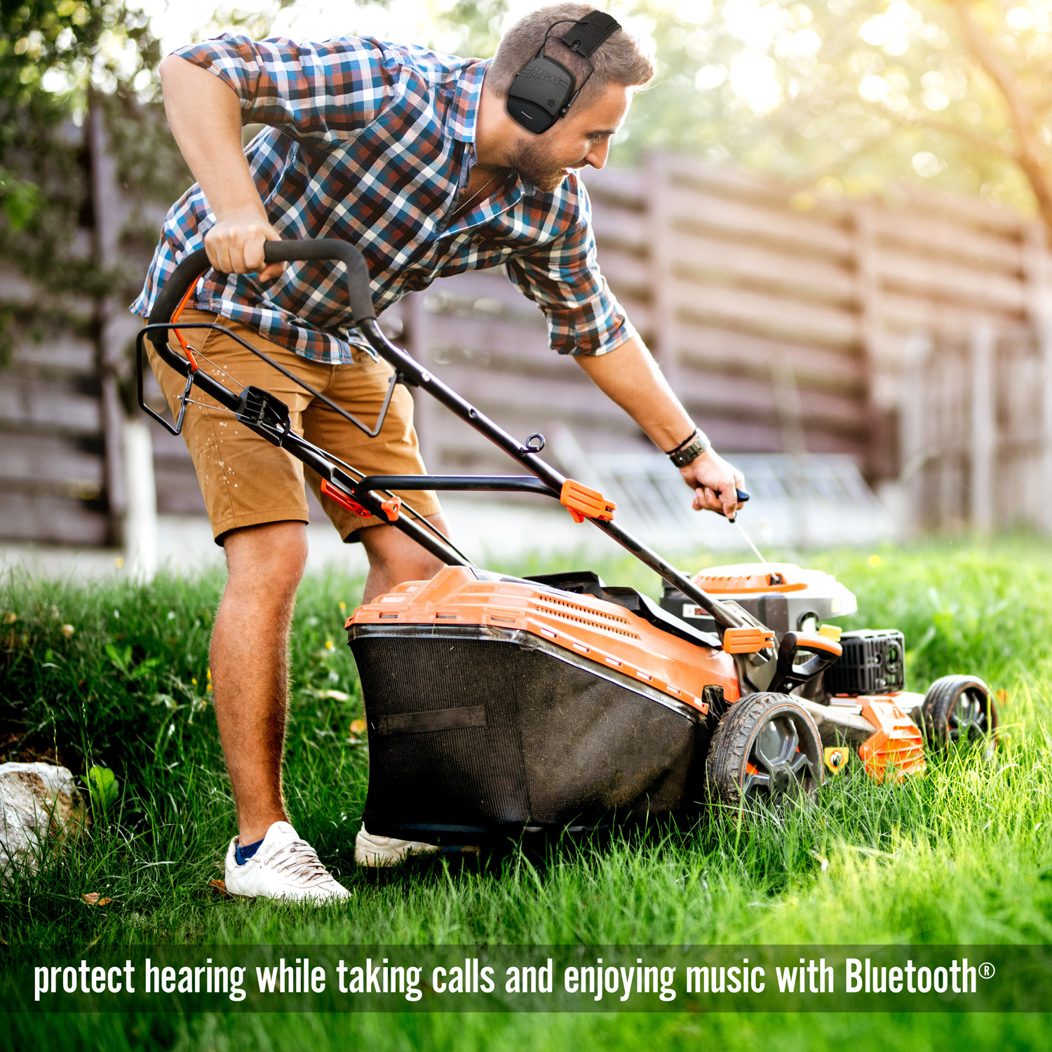 A person wearing Mack's Hearing Muffs with Bluetooth while mowing the lawn.
