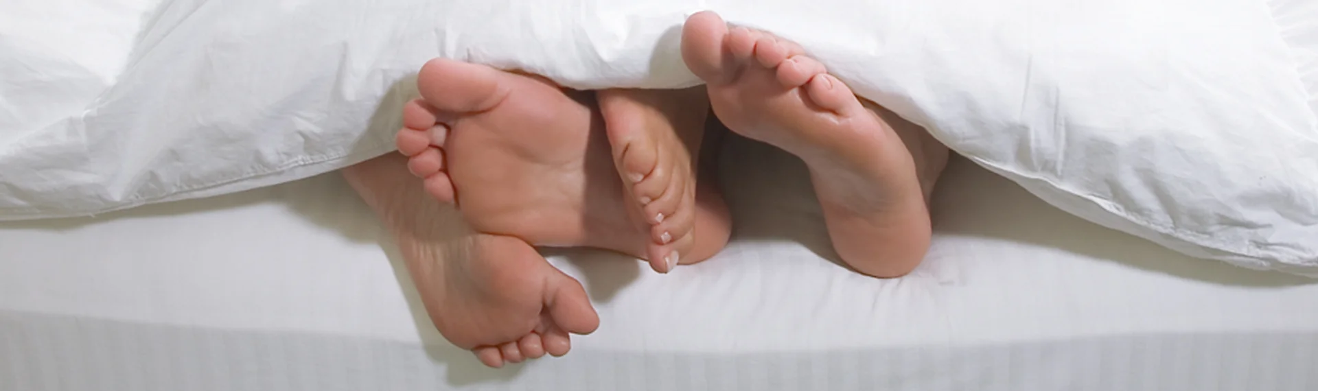 Sleeping ear plugs background image. Shows two pairs of feet on a bed